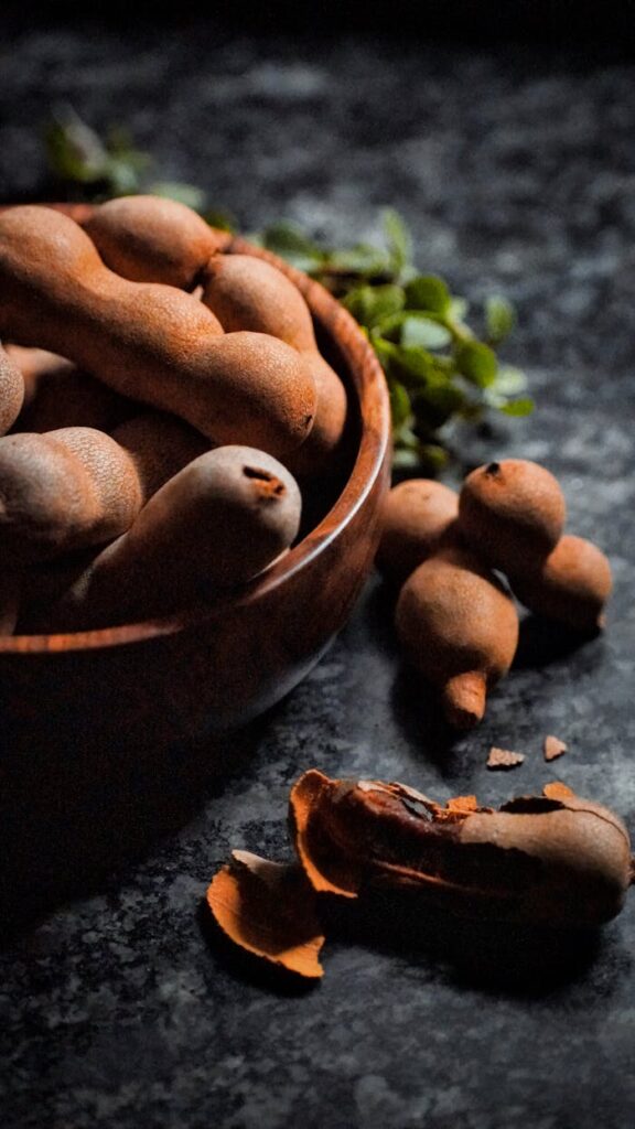 A rustic close-up of tamarind pods in a wooden bowl, showcasing their natural texture and earthy tones.